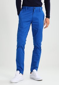 Modré chino kalhoty vyrobené z lehkého materiálu, s klasickým střihem, poutky na opasek a předním zapínáním. V kombinaci s bílými teniskami.