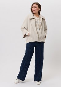 Beige cord jasje met een brede kraag en twee voorzakken over een crèmekleurige hoodie. Draag met losse, donkerdenim jeans en witte sneakers.