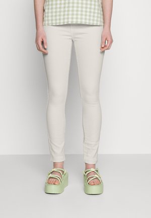 Jeans justos bege claro combinados com sandálias de plataforma verdes chunky, apresentando detalhes florais e várias tiras. Top com padrão não mostrado.