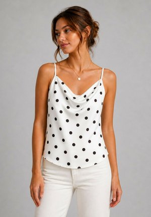Femme aux cheveux bruns en chignon bas portant un haut blanc sans manches à pois noirs et un pantalon blanc, regardant sur le côté.