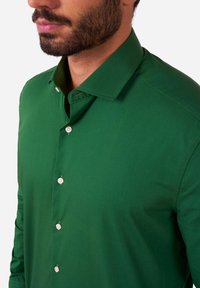 Camicia da uomo verde in cotone con colletto strutturato, pattina con bottoni arrotondati, vestibilità sartoriale e texture liscia.