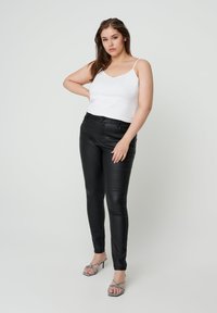 Zwarte nepleder broek met een slim fit, gecombineerd met een witte cami-top. Doorzichtige banden en versierde open teen hoge hakken.