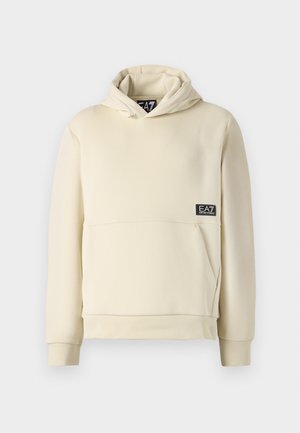 Cream-colored hoodie with a kangaroo pocket, drawstring hood, and branded patch on the lower front. Soft fabric and ribbed cuffs.