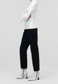 Biała strukturalna szyja, czarne spodnie z subtelnymi wzorami i białe botki za kostkę z metalowymi obcasami.