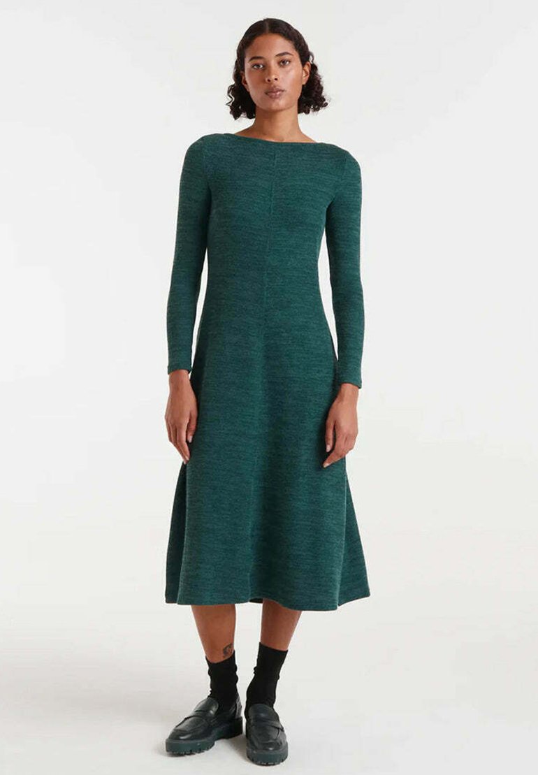 Vestido largo de manga larga en verde oscuro, hecho de una tela de punto texturizada, con escote barco y falda acampanada, combinado con calcetas y zapatos negros.