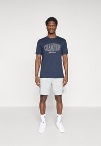 Marine-blaues Baumwoll-T-Shirt mit "CHAMPION"-Logo, kombiniert mit grauen Shorts, weißen Sneakers und weißen Socken mit Logo-Details. Einfache lässige Sportbekleidung.