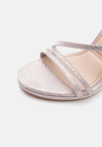 Prikaz izbliza bež sandale s dva tanka, teksturirana remena i uzorkom zmijskog kože na otvorenom dijelu prstiju i potplatu.