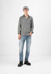 Camisa de cuadros en tonos grises, jeans azul claro y zapatos negros gruesos, combinados con una gorra gris. Outfit sencillo y casual.