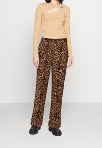 Beige långärmad topp med ett utskärningsdetalj, kombinerad med högmidjade bruna byxor med leopardmönster. Modellen bär svarta platåskor.