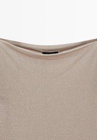 Tessuto a maglia beige scintillante con scollo piegato e una piccola etichetta nera parzialmente visibile al centro superiore.