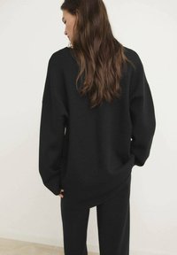 Schwarzer, übergroßer Strickpullover mit überschnittenen Schultern und langen Ärmeln, der eine weiche Textur und eine lockere Passform aufweist, kombiniert mit passenden schwarzen Hosen.