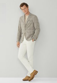 Jasnobrązowa marynarka w kratę z jednym guzikiem, w połączeniu z kremowymi slim-fit spodniami i tanowymi zamszowymi butami. Pod spodem prosta koszulka z okrągłym dekoltem.