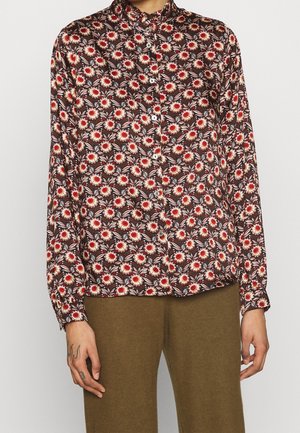 Langærmet skjorte med knapper med brun, rød og hvid blomsterprint, båret med olivengrønne bukser.