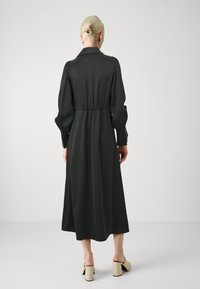 Dark green, long-sleeve dress with a cinched waist, full skirt, collar, and puffed sleeves. Worn with light-colored block-heeled sandals.