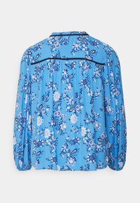 Blusa floral azul com mangas longas, detalhes franzidos nos ombros e acabamentos pretos na parte de trás do ombro. Tecido leve e texturizado com padrões de flores.