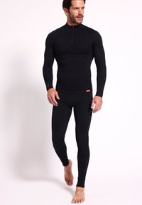 Camiseta de base de manga larga negra con cremallera y leggings a juego. La tela tiene un patrón texturizado, diseñada para uso atlético.
