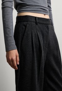 Pantaloni a pieghe grigio ardesia con una morbida texture, dotati di una vita e dettagli di cucitura discreti, abbinati a un top aderente a maniche lunghe.