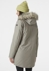 Parka aislante de color gris claro con capucha decorada con piel. Presenta una cintura ajustada, mangas largas y un gorro de punto en color verde claro con canalé.