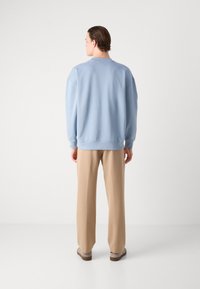 Sudadera de gran tamaño en azul claro, con puños y dobladillo acanalados, combinada con pantalones de pierna ancha en color beige. Textura suave, diseño minimalista y sin patrones.