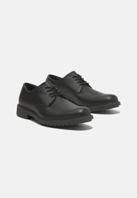 Scarpe in pelle nera con punta arrotondata, design con lacci e suola in gomma testurizzata. Presentano un dettaglio del logo discreto sul lato.