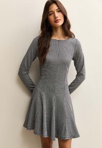 Zwart-witte hondenbotjesshirtjurk met lange mouwen, nauwsluitend lijfje, uitlopende rok en ronde halslijn. Gemaakt van een gestructureerde stof.