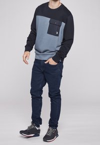 Mörkblå och ljusblå sweatshirt med framficka, kombinerad med blå jeans och grå sportskor. Mjuk textur, avslappnad design.