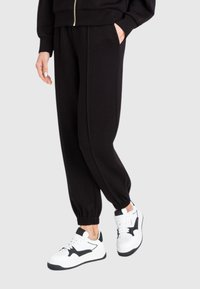 Pantaloni da tuta neri con polsini elasticizzati, tasche laterali e vestibilità comoda, abbinati a sneakers bianche con un accento di design nero.