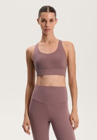 Mauve športni modrček in visoko pasne legice iz gladkega, raztegljivega materiala. Modrček ima široke naramnice in poenostavljen dizajn.