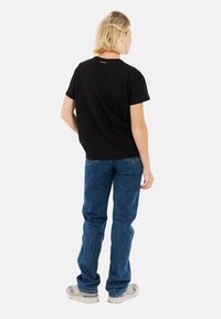 Zwarte katoenen t-shirt met korte mouwen, een ronde hals, en een subtiele logo op de achterkant, gecombineerd met losse blauwe denim jeans en grijze sneakers.