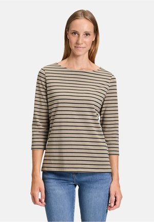 Beige top met driekwartmouwen en zwarte horizontale strepen. Heeft een bateauhals en zachte, rekbare stof. Gepaard met lichtblauwe jeans.
