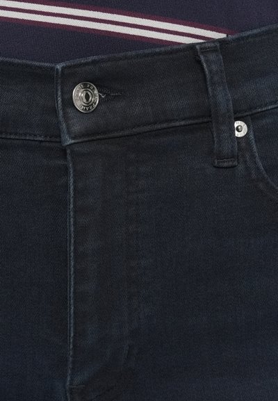 Tumedad denimist teksapüksid, millel on silmapaistev sile tekstuur, hõbedase metallist nööbiga kinnis ja nähtavad õmblused vöökohal.