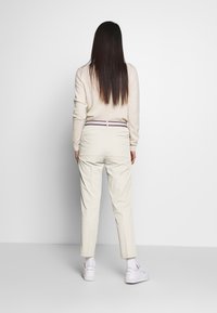 Pantaloni beige chiaro con vita attillata e gambe affusolate, caratterizzati da un colore solido e un accento a righe sulla cintura. Design per abbigliamento casual.
