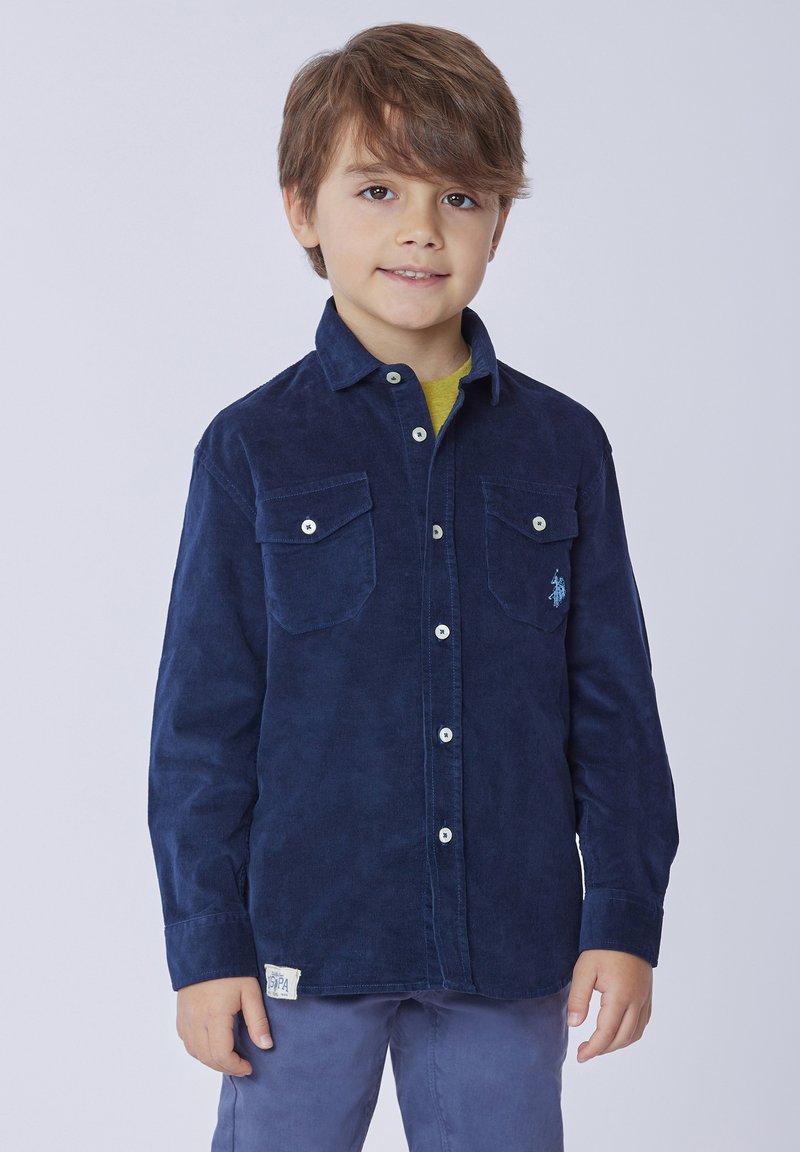 Camicia di velluto a coste blu navy con colletto button-down, due tasche sul petto, bottoni bianchi e un piccolo logo ricamato su una tasca.