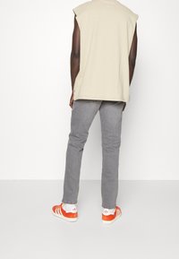 Top sin mangas beige, pantalones grises y zapatillas con rayas naranjas. El top tiene un ajuste holgado y los pantalones son ajustados con una textura suave.