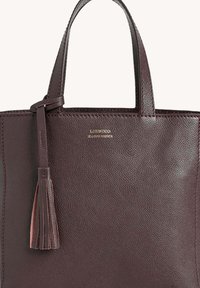 Sac fourre-tout en cuir texturé marron foncé avec doubles poignées et un charm en cuir assorti attaché sur le côté gauche.