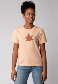 Pfirsichfarbens Baumwoll-T-Shirt mit kurzen Ärmeln, das ein geometrisches rotes Ahornblatt-Muster in der Mitte aufweist. Klassischer Rundhalsausschnitt.