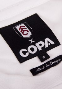 Witte stoffen label met zwart en rood logo "FFC" en "COPA." Bevat de maat "S" en de tekst "Gemaakt in Europa." Vlak, rechthoekige vorm.