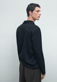 Zwarte lange mouw polo met een klassieke kraag, met een gladde textuur en een relaxte pasvorm, gecombineerd met donkere broeken.