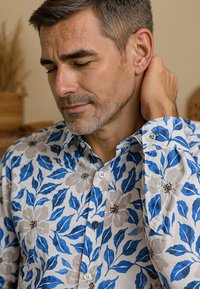 Witte blouse met een patroon van blauwe bladeren en grijze bloemen, met een button-down kraag en lange mouwen met knopen aan de manchetten.