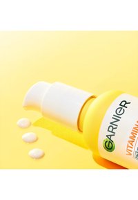 Gul Garnier Vitamin C cremeflaske med hvid pumpe og tre klatter creme på gul overflade.