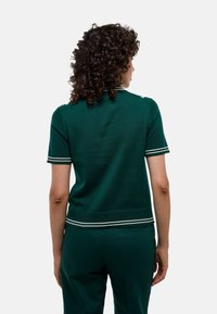 Polo vert à manches courtes avec des accents de rayures blanches sur le col et l'ourlet, confectionné en tissu tricoté lisse.