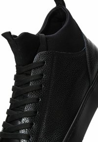 Czarne sneakersy z teksturowanej skóry i gładkiego materiału, charakteryzujące się zaokrąglonym kształtem, sznurowanym przodem i kontrastującą matową gumową podeszwą.