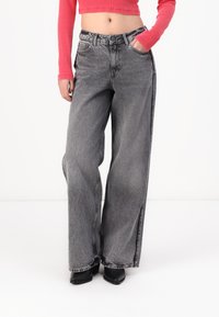 Pelni augsto vidukli ar plašām kājām džinsi pelēkā denimā ar izbalējumu, iekļaujot priekšējās kabatas un sānu šķēlēs apakšā. Melni platformas apavi.