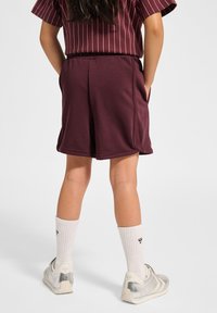 Bordeauxfärgade shorts med elastisk midja, sidofickor och mjukt material; tillsammans med vita knälånga strumpor och sneakers i silverfärg.