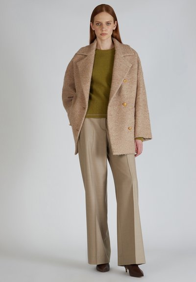Beige wollen blend dubbele breasted jas met textuurafwerking, gecombineerd met een groene gebreide sweater en beige broek met wijde pijpen.