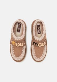 Smeđe suede cipele na slip-on s mekanim podstavljanjem, pletenim detaljima i zlatnim logotipom. Mekana tekstura i zaobljen oblik.