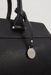 Sac à main en cuir noir texturé avec doubles poignées et une étiquette de marque ronde en argent portant l’inscription « L.CREDI MUNICH bags since 1954 » sur une bandoulière en cuir.