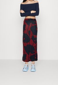 Top bez ramínek v námořnické modři, spárovaný s dlouhou červenou sukní se černým kv ětinovým vzorem. Modré sandály na pásky dotvářejí celkový vzhled.