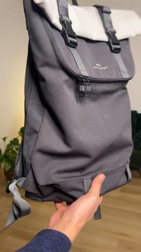 Mochila de tela gris oscuro con cierre enrollable blanco y correas ajustables. Cuenta con un bolsillo con cremallera y detalles laterales de malla.