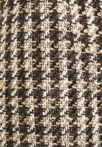 Texturerad tyg som har en blandning av bruna, beige och vita garntrådar, med ett vävt mönster som skapar djup och kontrast.